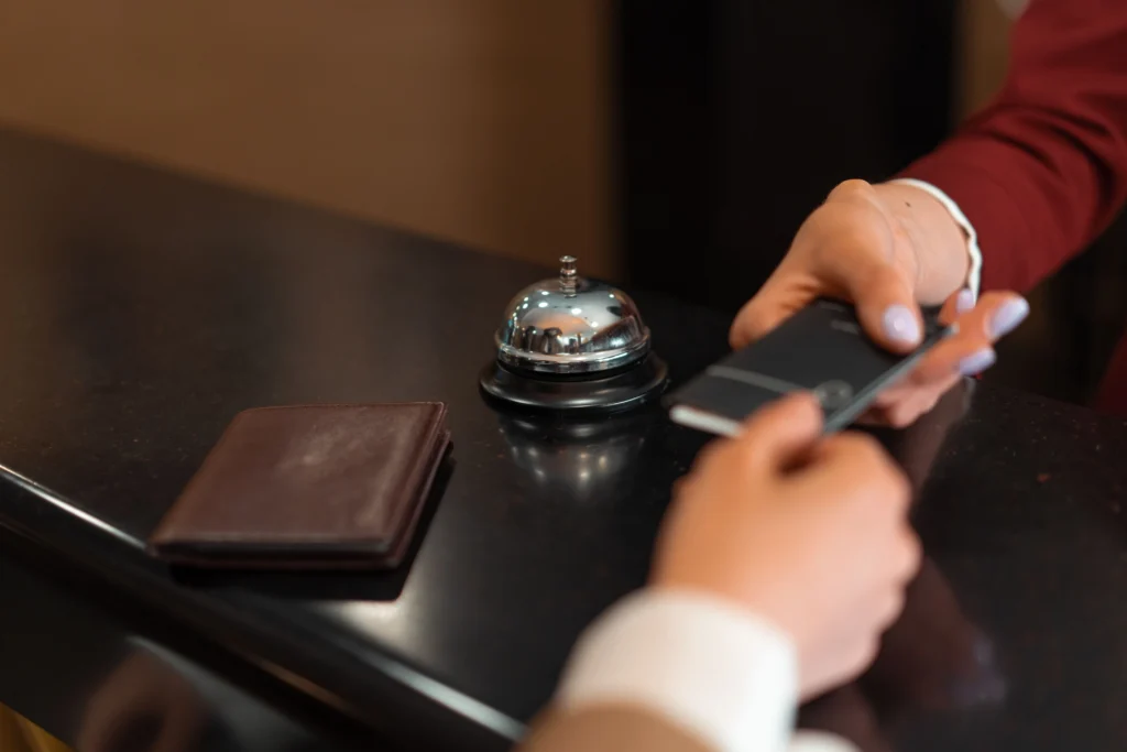 a ring-bell on counter top table and someone handing access room card