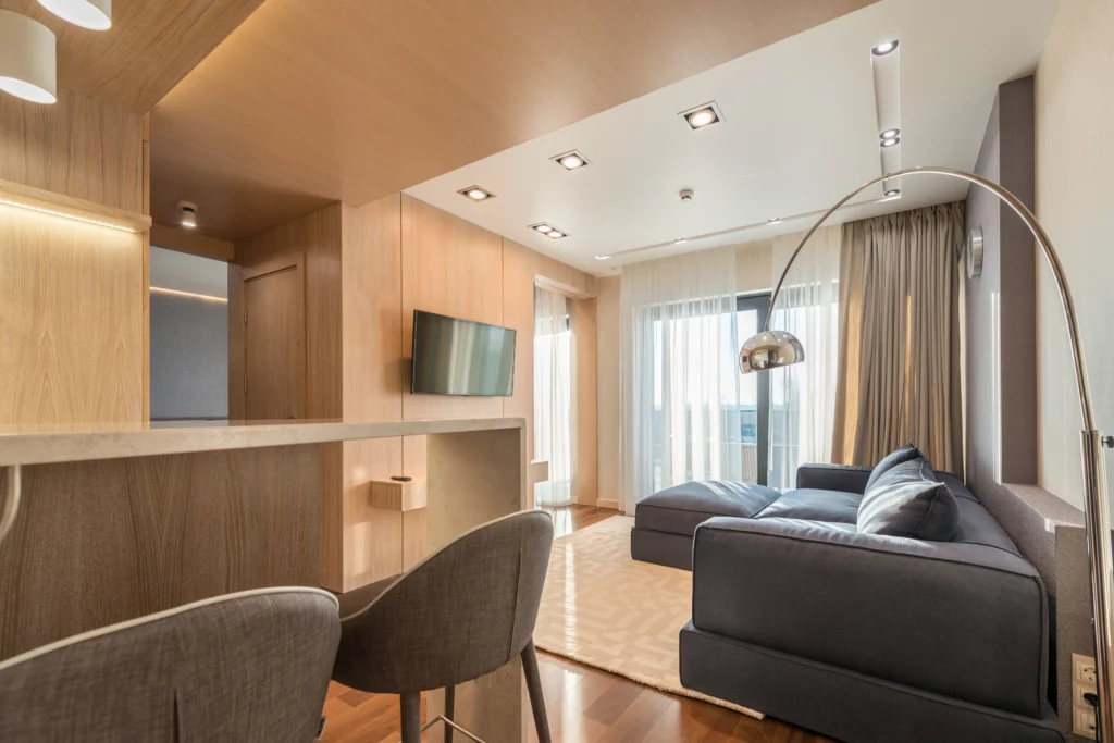 a room with big stools and big sofa, television and big window